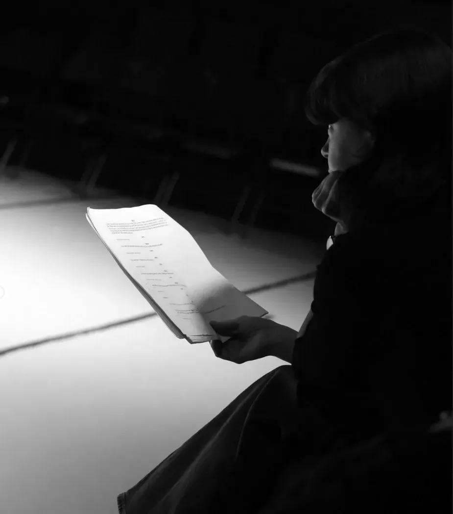 A performer reads a script in a darkened theatre